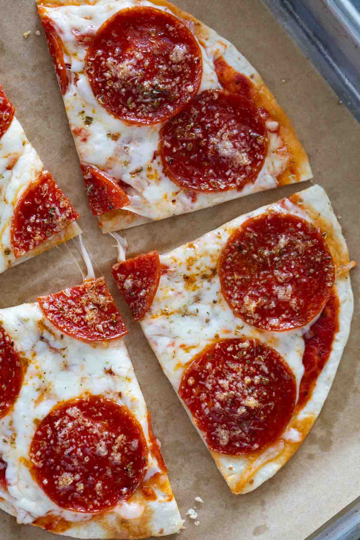 Tortilla Pizza cut into slices on a baking sheet, topped with cheese and oregano.