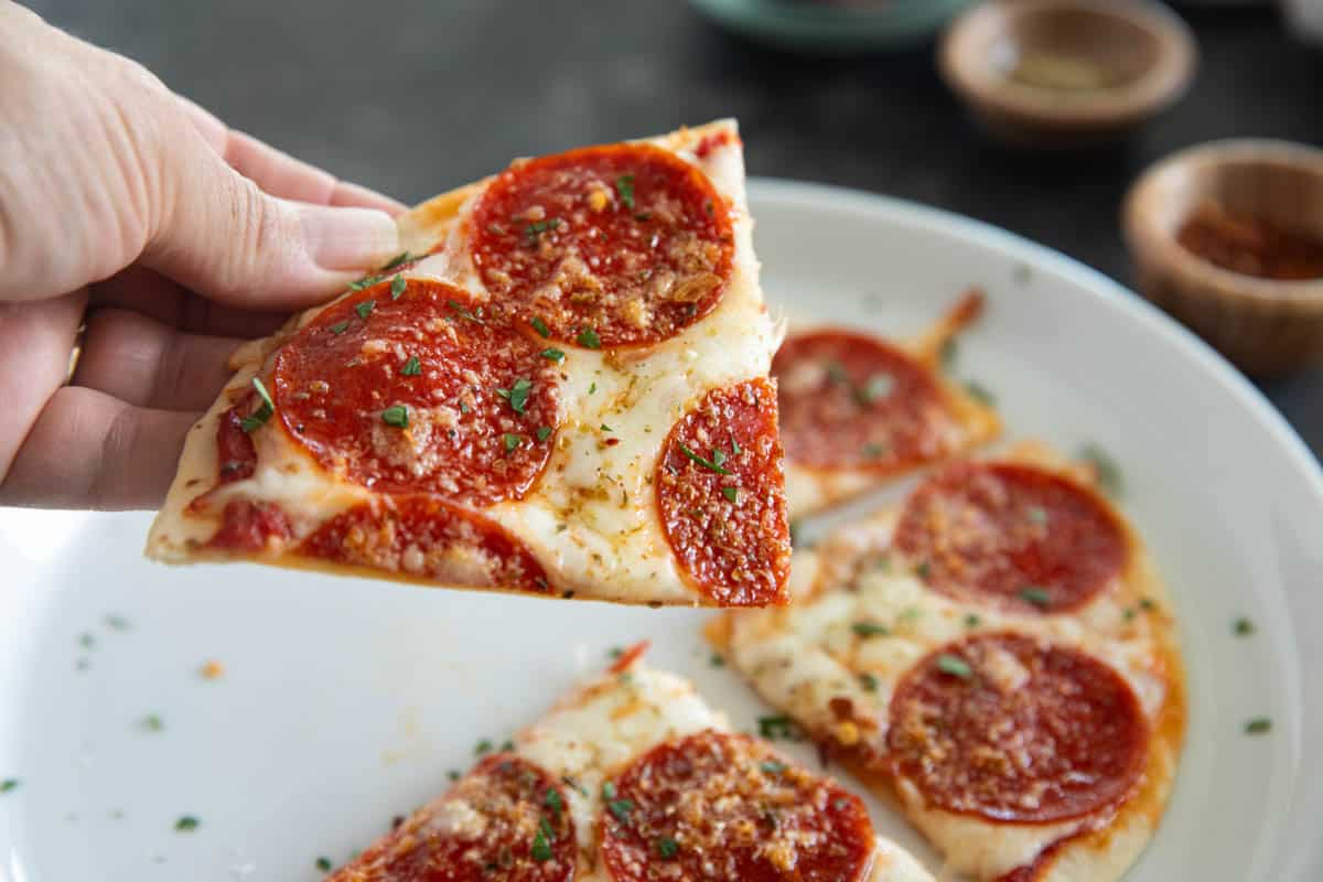 Hand holding a slice of tortilla pizza.