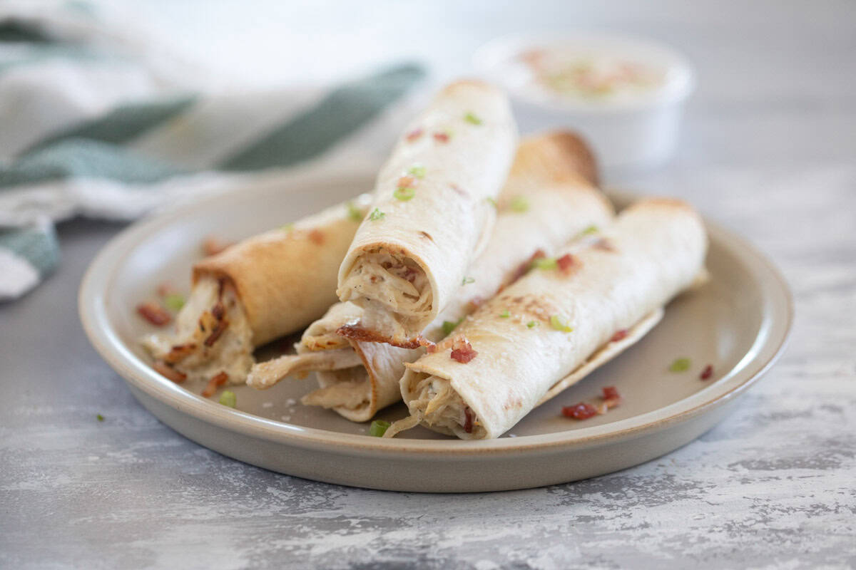 Four Baked Chicken Bacon Ranch Taquitos on a plate with sliced green onions and bacon crumbles.