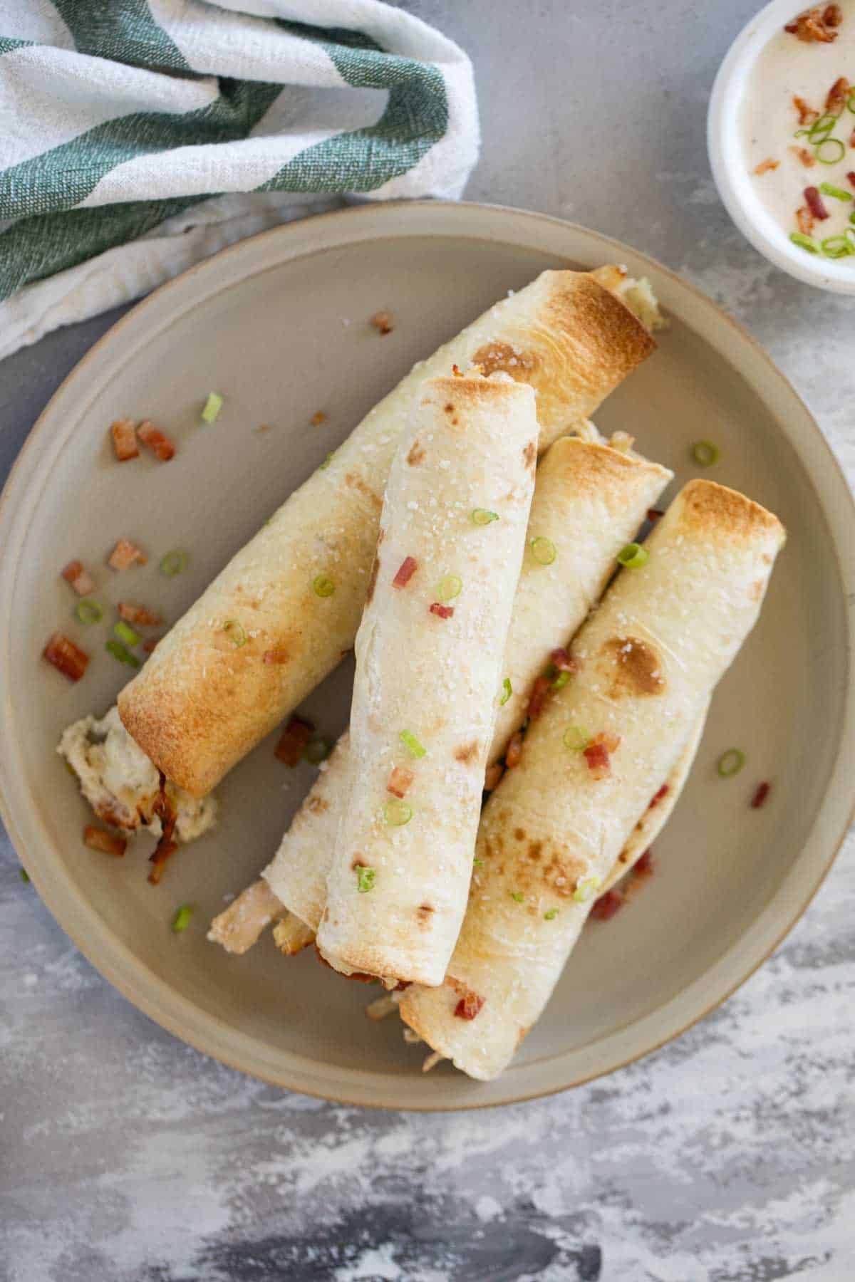 Baked Chicken Bacon Ranch Taquitos with green onions and salt on top.