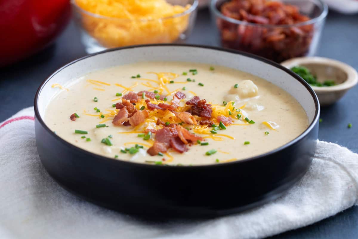 Bowl full of baked potato soup, topped with cheese and bacon.