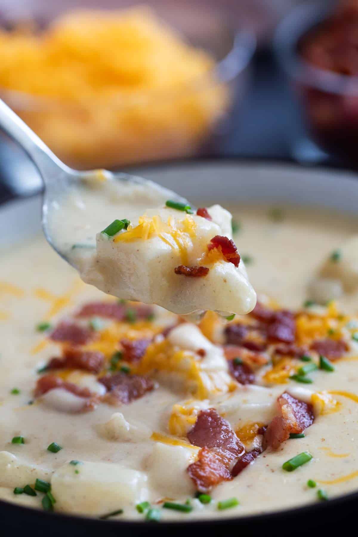 Spoon filled with baked potato soup, topped with bacon and cheese.