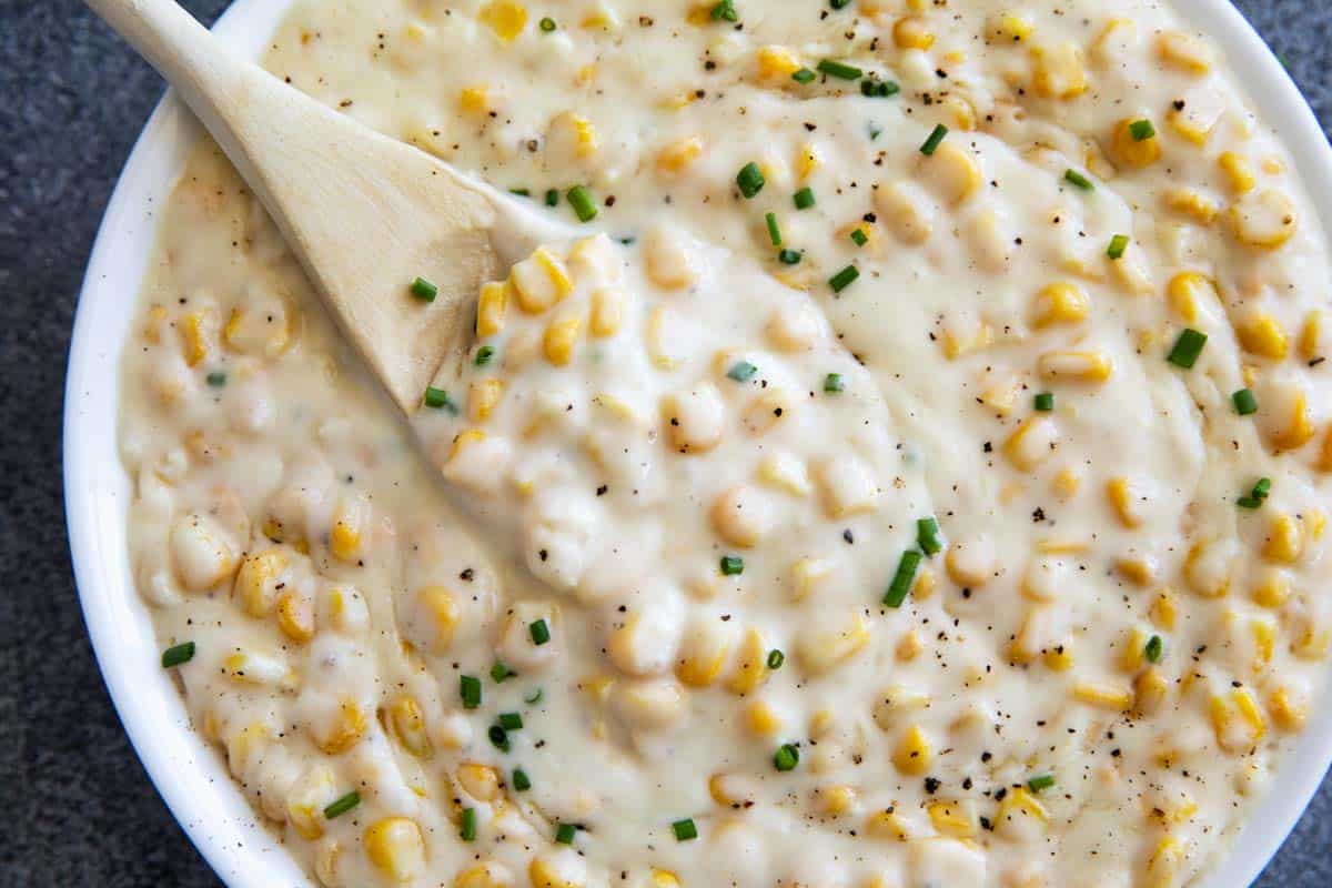 Creamed corn in a bowl with a wooden spoon.