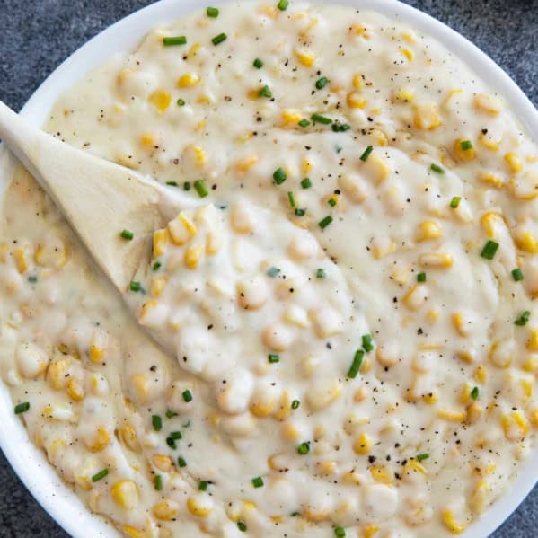 Creamed Corn topped with pepper and chives in a white serving bowl.