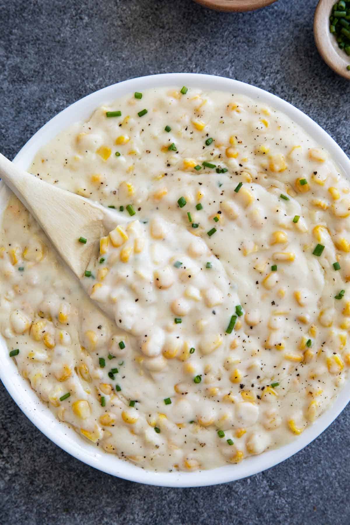 Creamed Corn topped with pepper and chives in a white serving bowl.