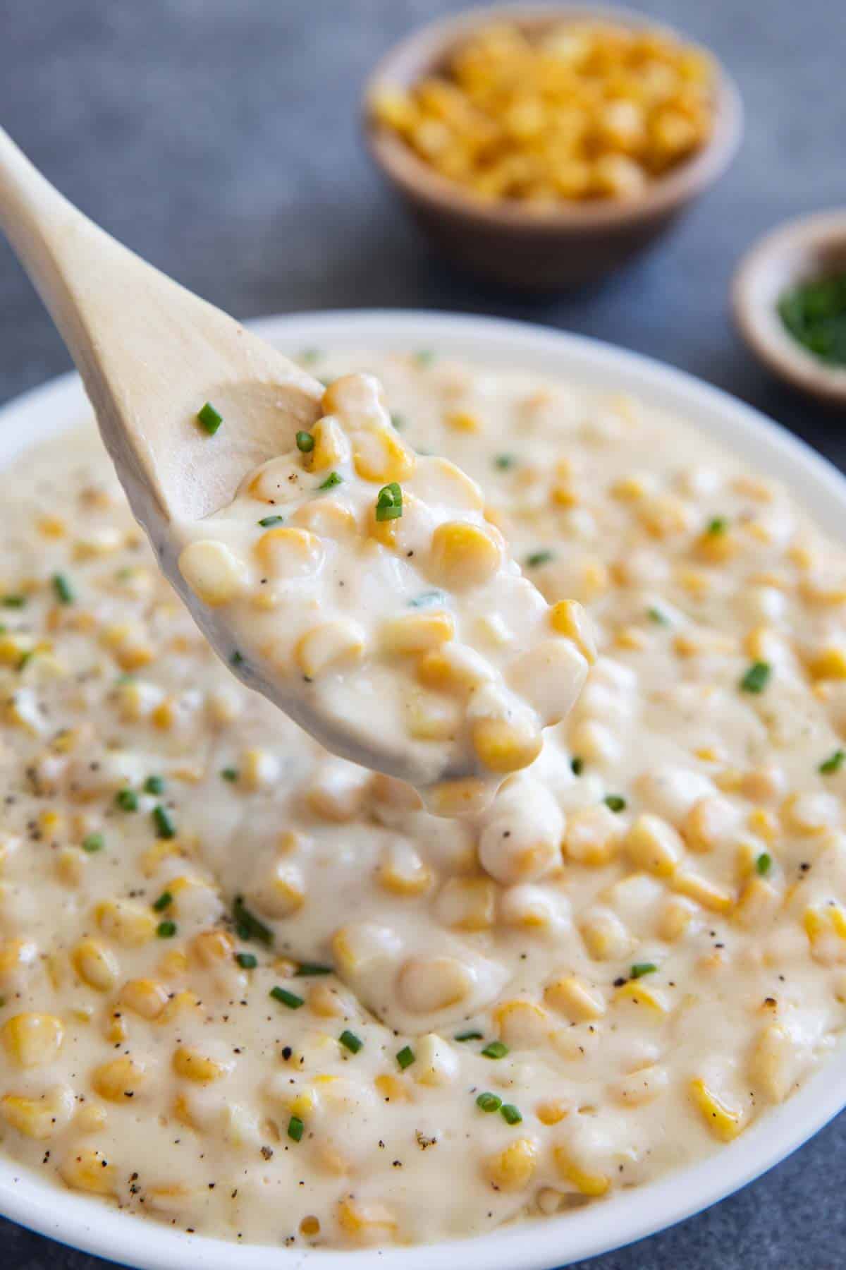 Wooden spoon scooping out creamed corn topped with chives.