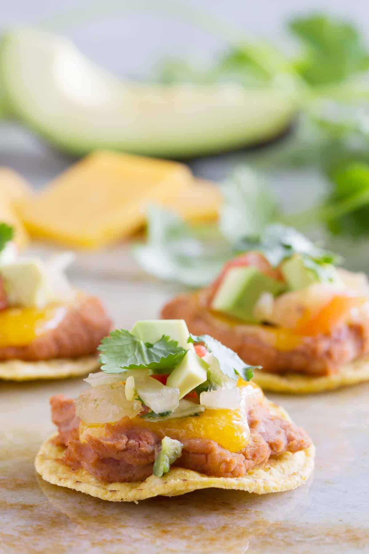 Nacho bites with a tortilla chip topped with refried beans, cheese, and toppings.