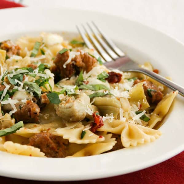 Pasta with Sausage, Artichokes, and Sun-Dried Tomatoes in a bowl, topped with fresh basil and parmesan.