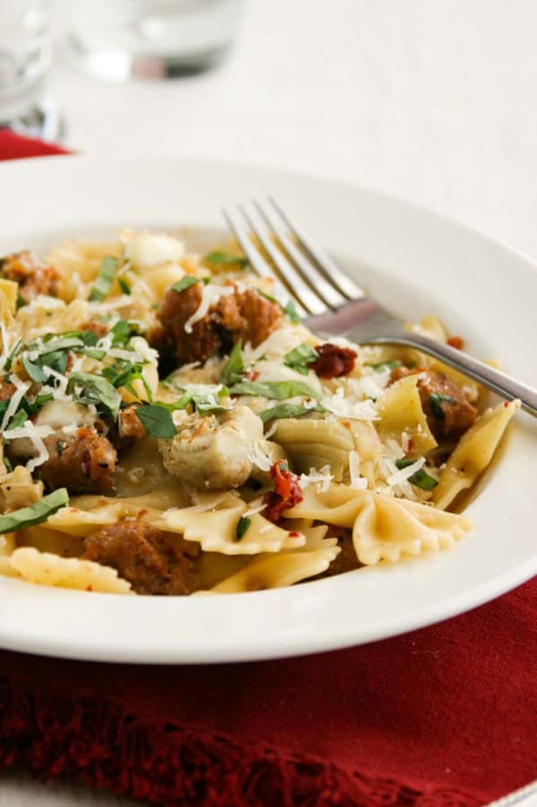 Pasta with Sausage, Artichokes, and Sun-Dried Tomatoes in a bowl, topped with fresh basil and parmesan.