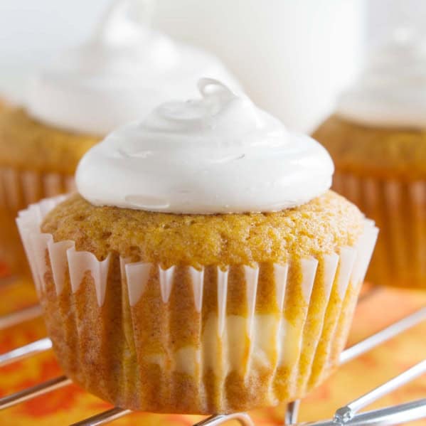 Pumpkin Cheesecake Cupcakes on a cooling rack over an orange cloth.