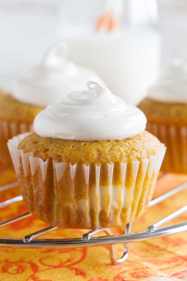 Pumpkin Cheesecake Cupcakes on a cooling rack over an orange cloth.