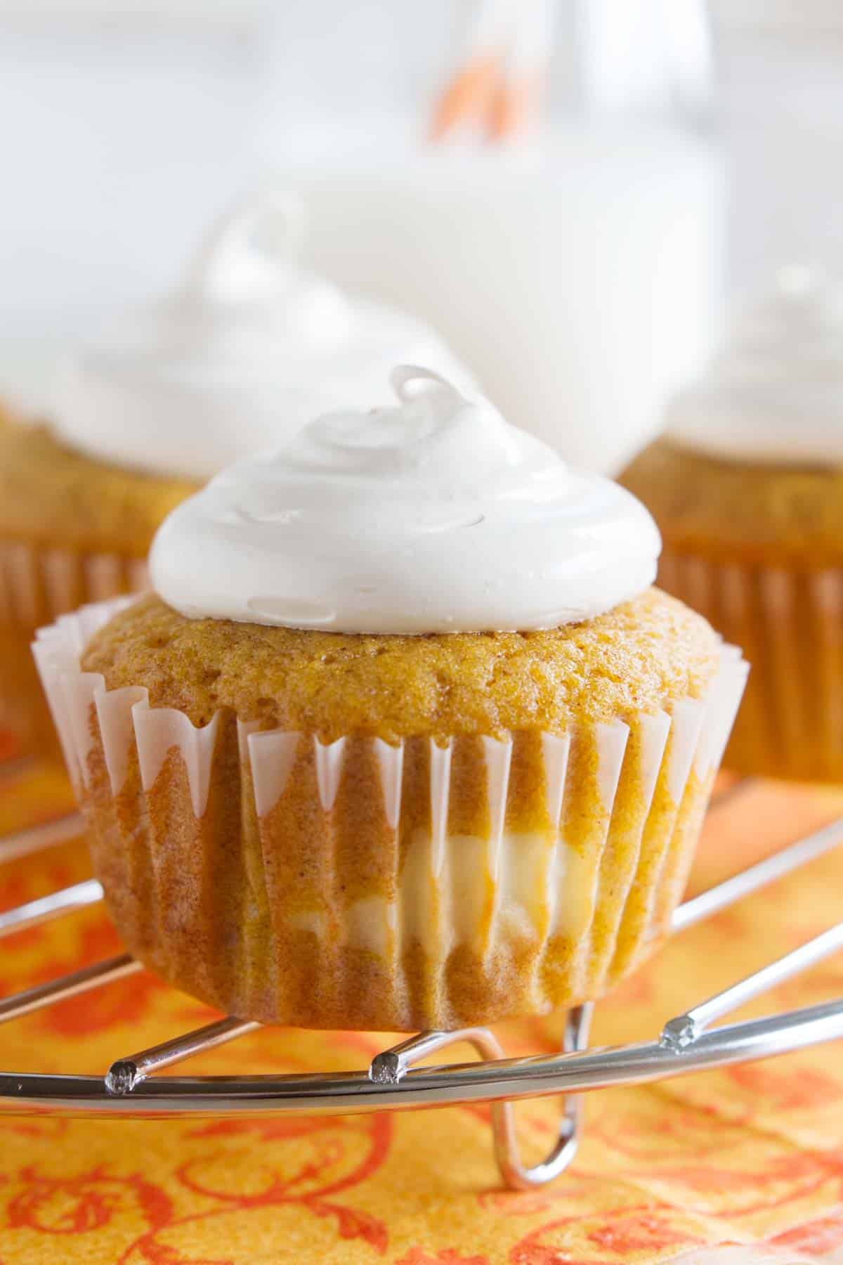 Pumpkin Cheesecake Cupcakes on a cooling rack over an orange cloth.