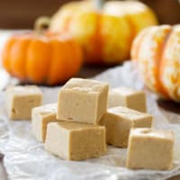 Squares of pumpkin fudge stacked with pumpkins in the background.