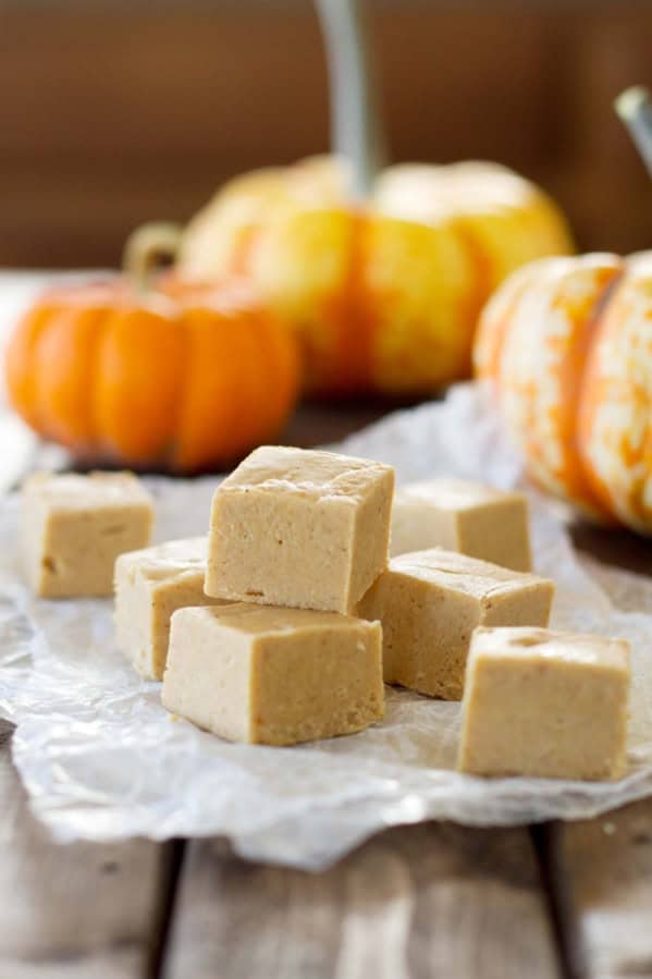 Squares of pumpkin fudge stacked with pumpkins in the background.