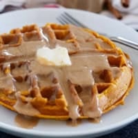 Pumpkin Waffles on a white plate topped with cinnamon syrup.