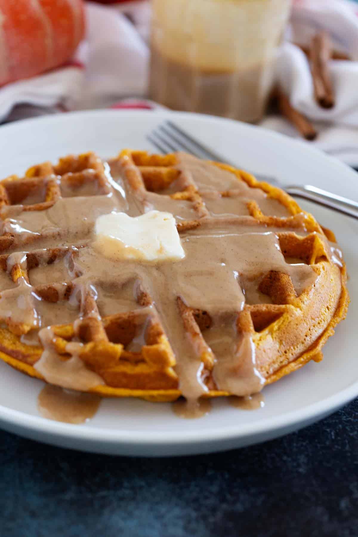 Pumpkin Waffles on a white plate topped with cinnamon syrup.