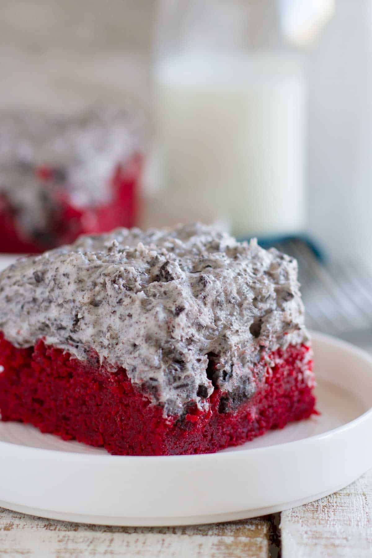 Slice of red velvet sheet cake with cookies and cream frosting on a white plate.