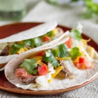 Slow Cooker Mexican Pork Roast Tacos topped with cheese and cilantro on a plate.