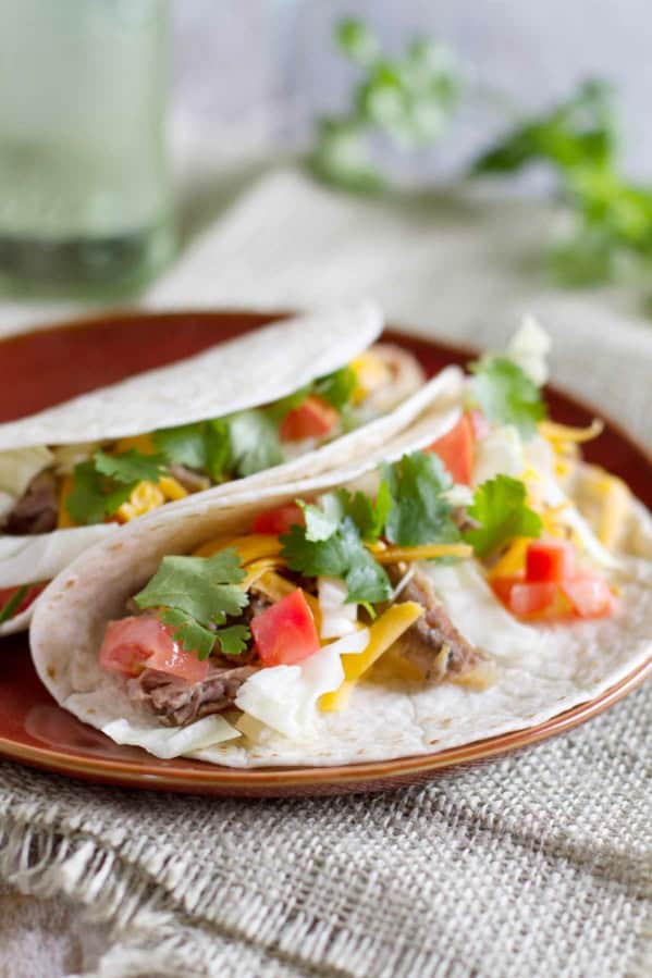 Slow Cooker Mexican Pork Roast Tacos topped with cheese and cilantro on a plate.