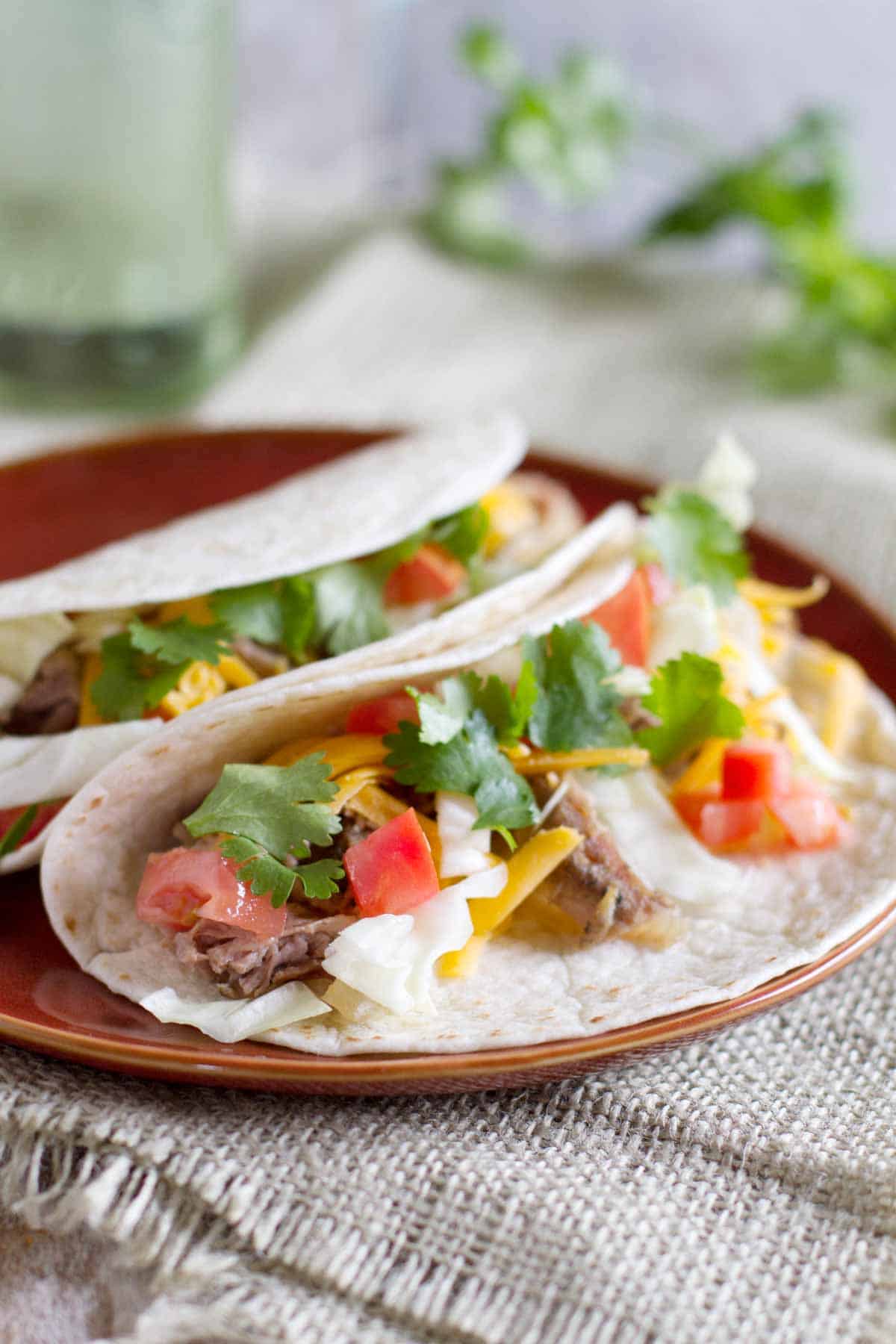 Slow Cooker Mexican Pork Roast Tacos topped with cheese and cilantro on a plate.