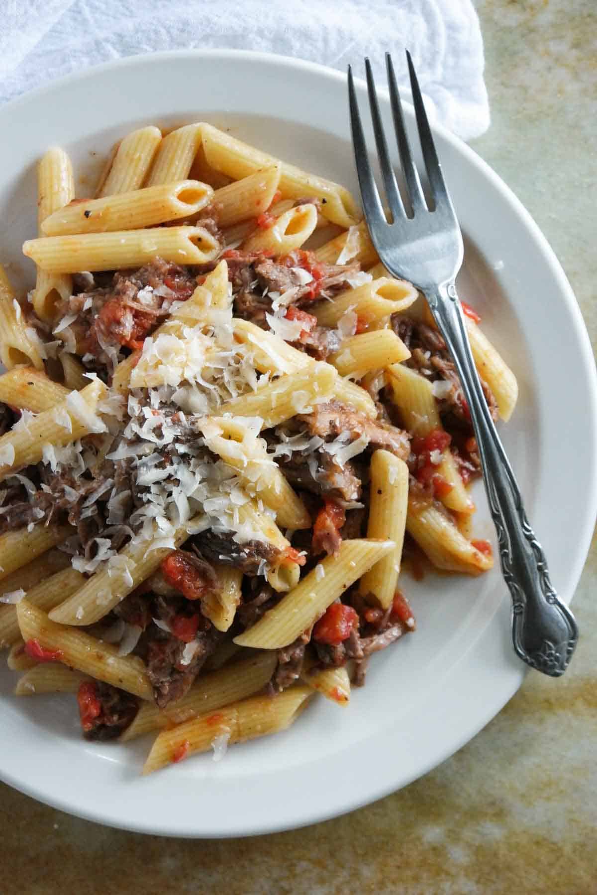 Plate filled with slow simmered short rib sauce with pasta with parmesan on top.