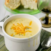 Bowl of cheesy vegetable chowder topped with cheddar cheese.