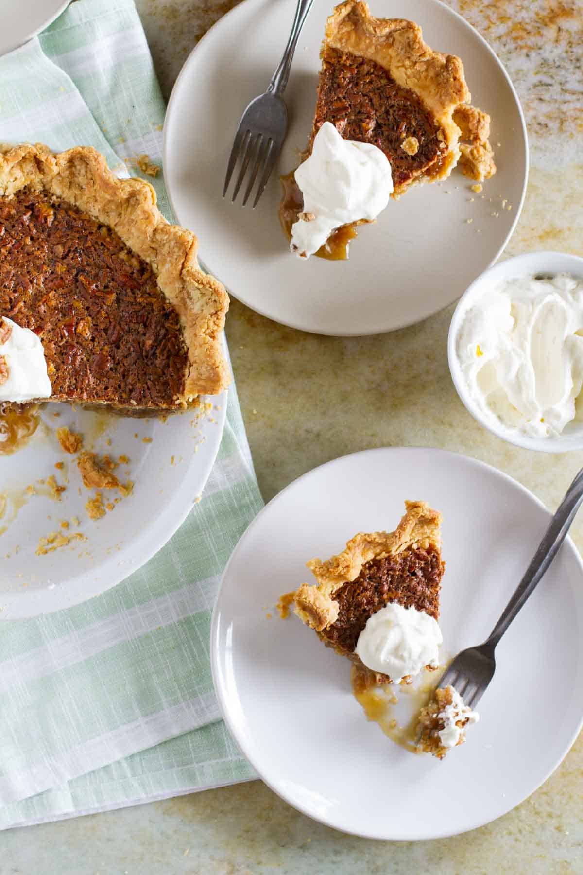 Slices of coconut pecan pie on plates, topped with whipped cream.