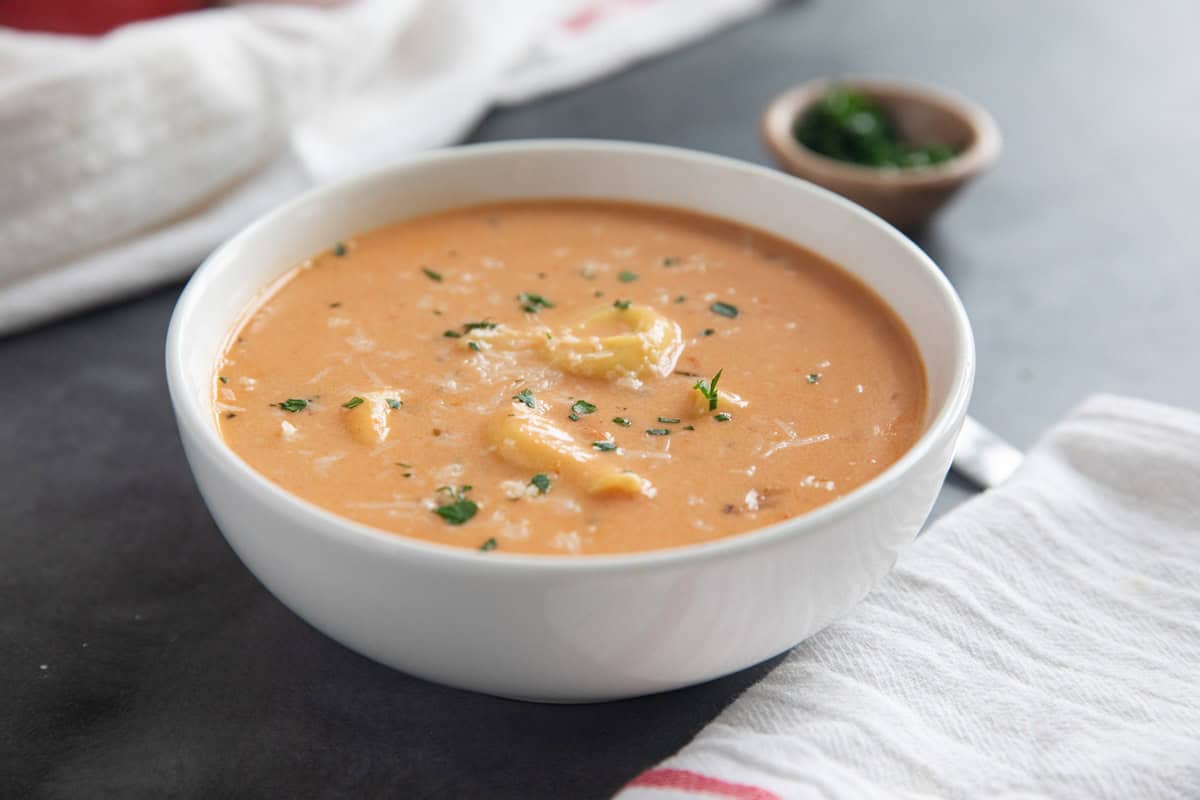 Bowl of creamy tortellini soup, topped with parmesan and herbs.