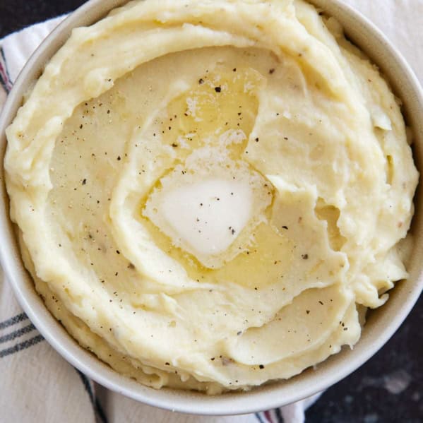 Bowl of Crockpot Mashed Potatoes topped with a pat of butter and pepper.