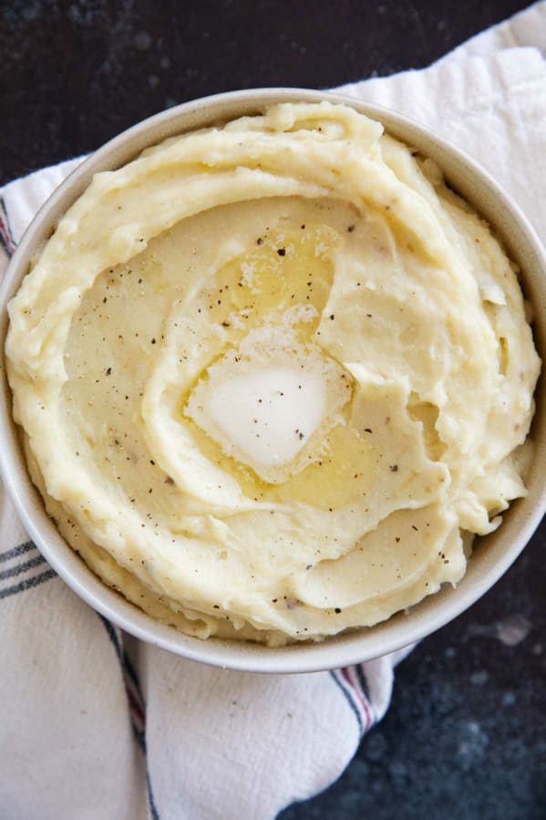 Bowl of Crockpot Mashed Potatoes topped with a pat of butter and pepper.