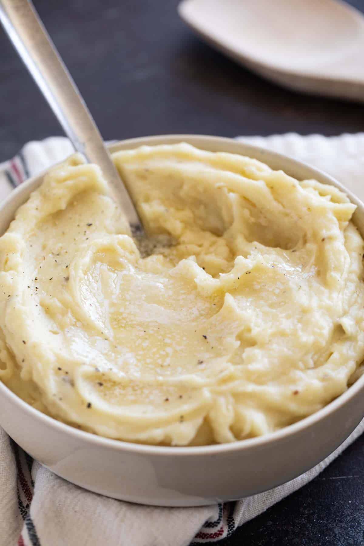 Bowl of crockpot mashed potatoes topped with butter, with a spoon in it.