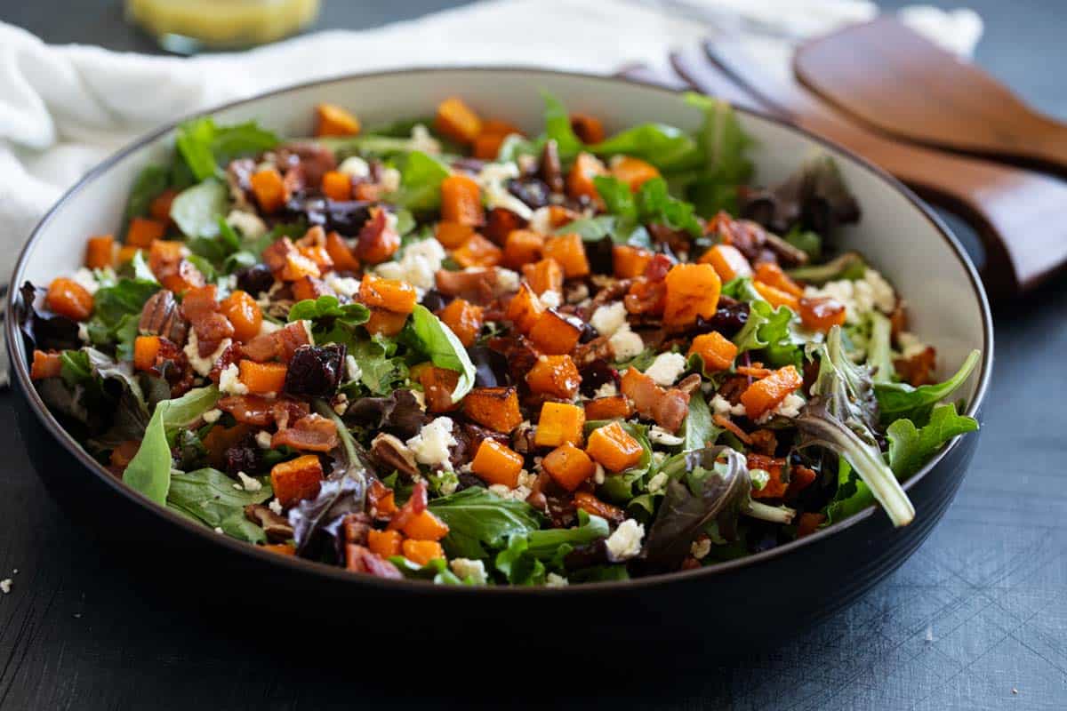 Bowl filled with Fall Harvest Salad, topped with roasted butternut squash and feta cheese.