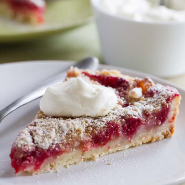 Slice of pear and raspberry tart, topped with whipped cream.