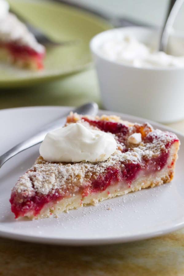 Slice of pear and raspberry tart, topped with whipped cream.