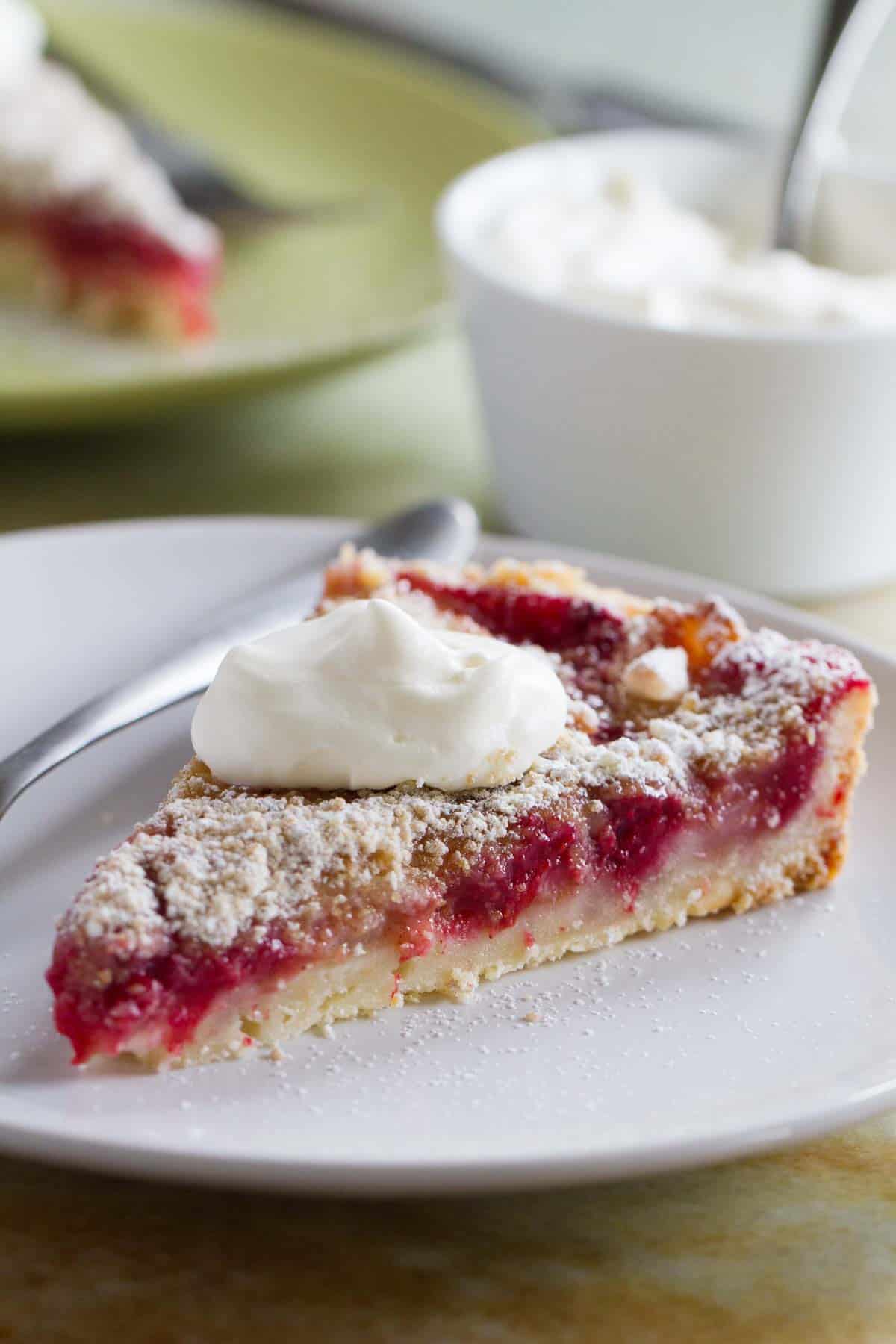 Slice of pear and raspberry tart, topped with whipped cream.