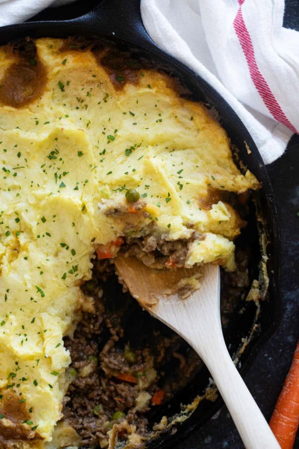 Cast iron skillet with Shepherd's Pie with aa wooden spoon.