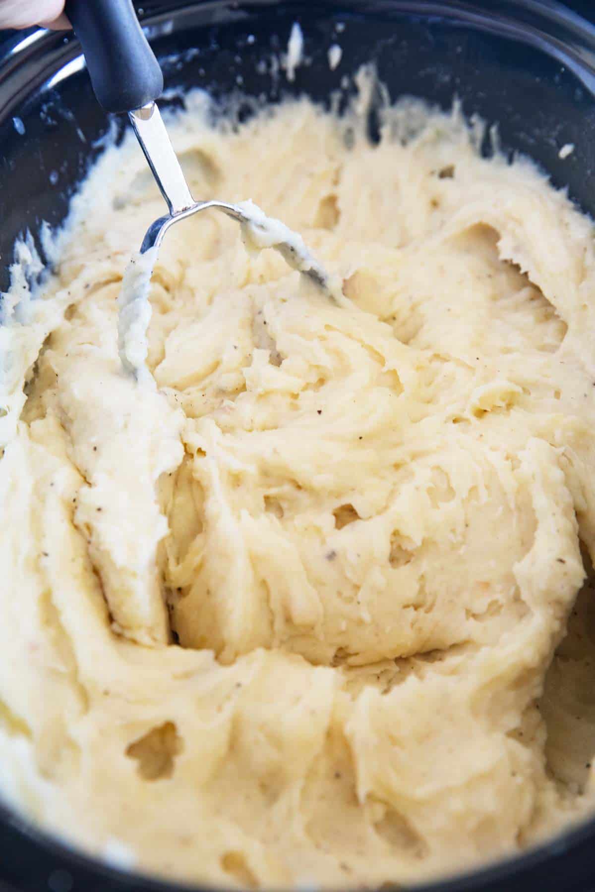 Mashed potatoes in the crock pot with a masher.