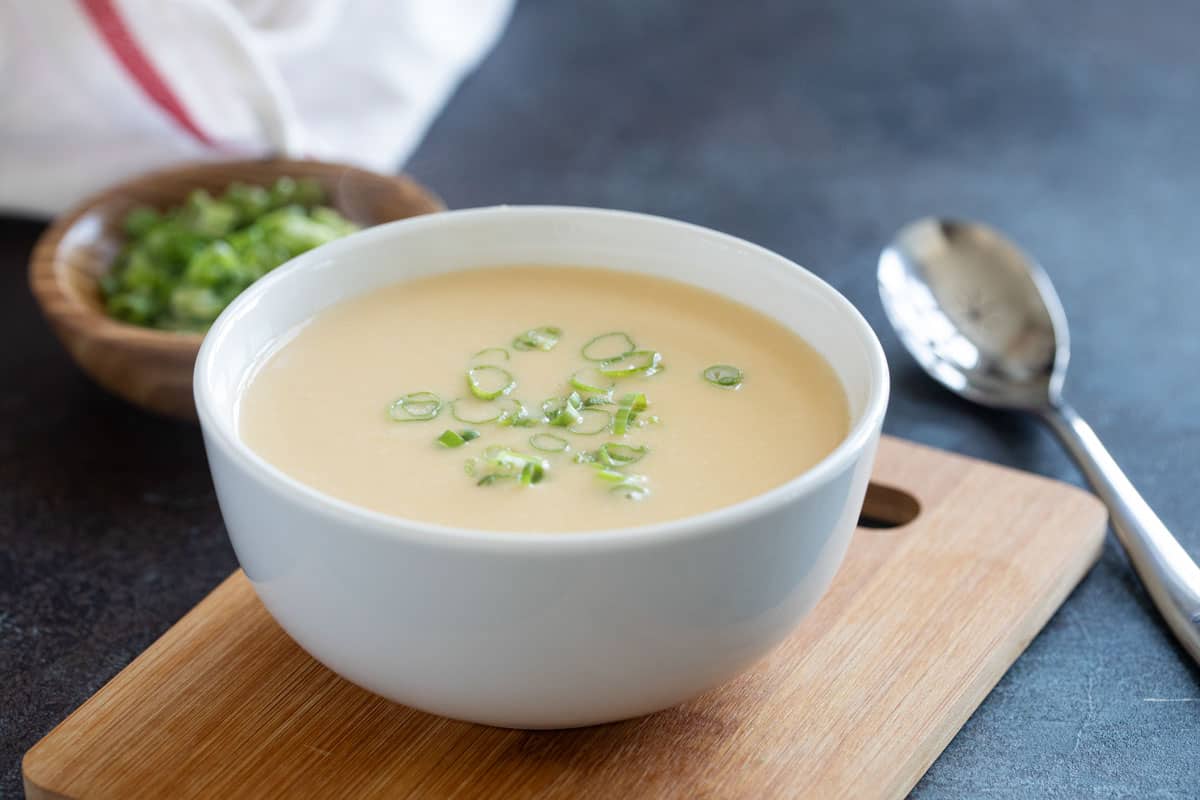 Bowl of Cheddar Cheese Soup with a spoon and green onions in the background.