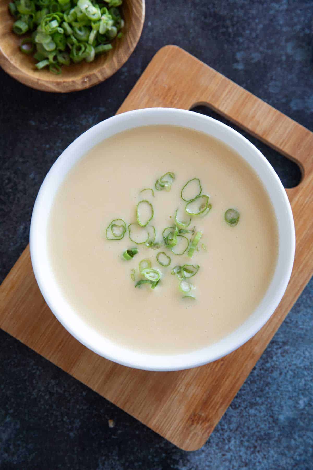 Bowl of Cheddar Cheese Soup on a wooden cutting board.