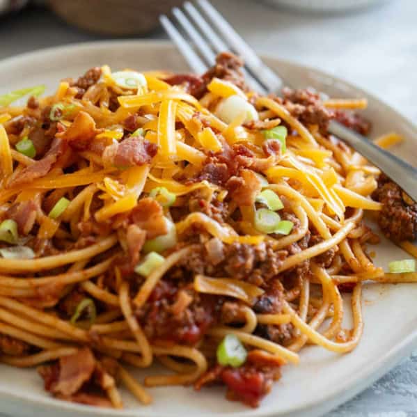 Plate of Cowboy Spaghetti with ground beef, bacon, cheese, and green onions.