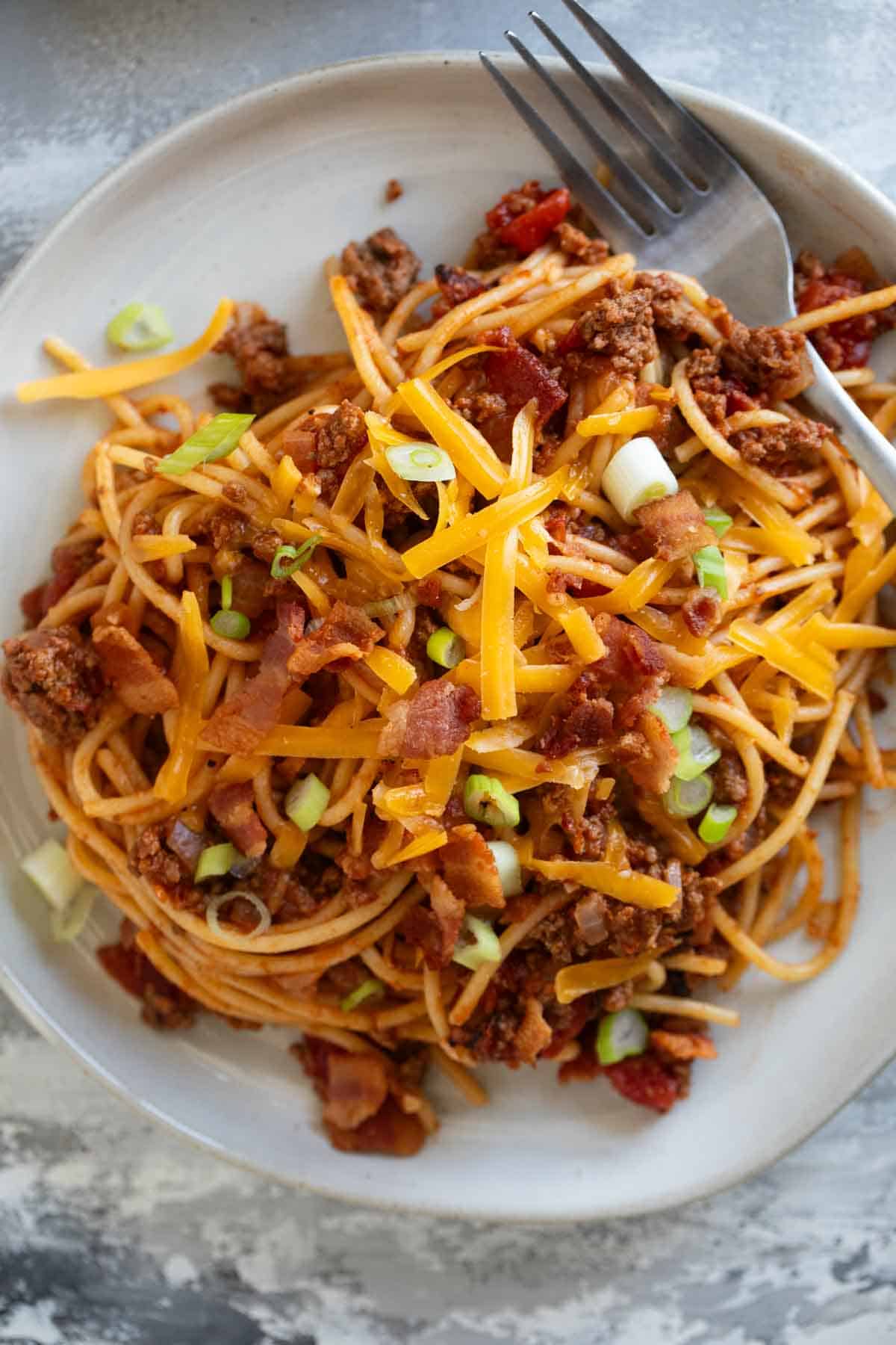 Plate full of Cowboy Spaghetti topped with shredded cheddar cheese.