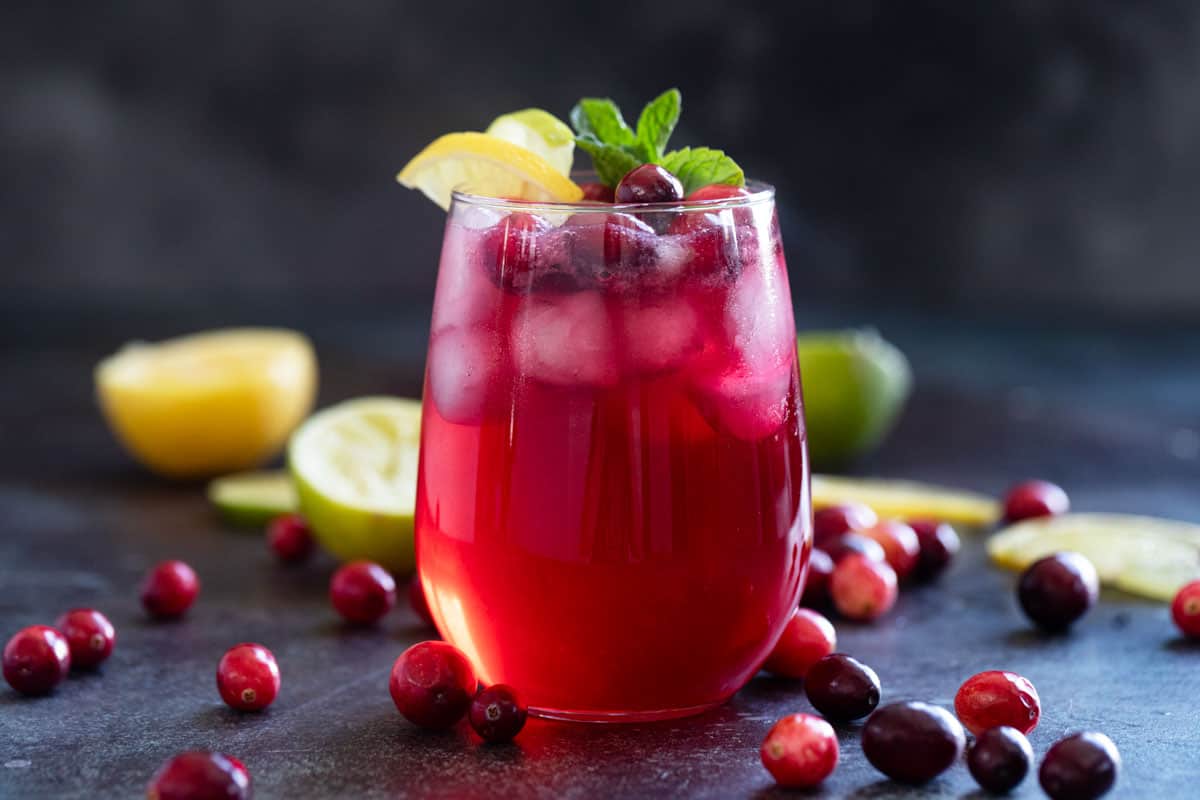 Cranberry spritzer in a clear glass with fresh cranberries and lemons and limes.