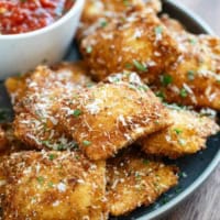 Fried Ravioli on a plate, sprinkled with parmesan and parsley.