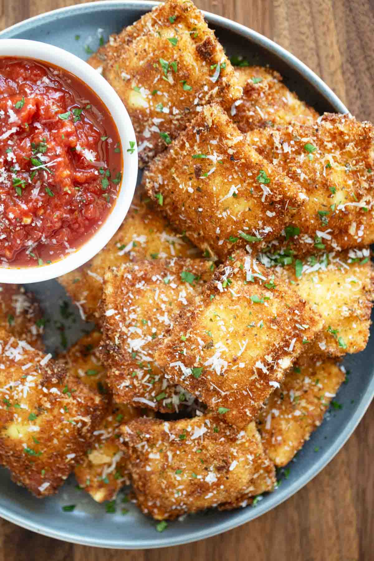 Plate filled with Fried Ravioli with a bowl of marinara sauce on the plate.