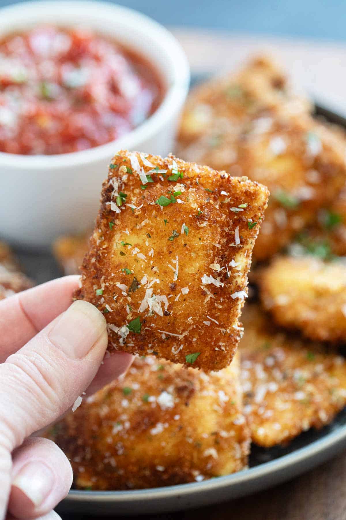 Holding a single fried ravioli up in front of a plate full of ravioli.