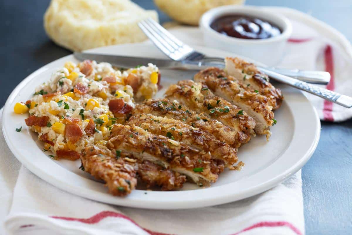 Sliced piece of Potato Chip Chicken served with corn and bbq sauce.