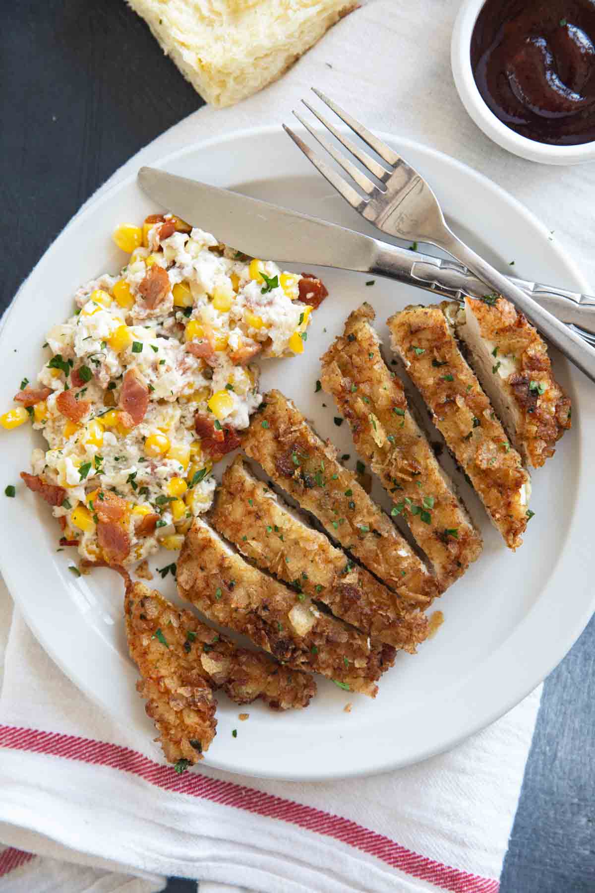 Sliced piece of Potato Chip Chicken on a plate with corn and bacon casserole.