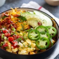 Loaded breakfast bowl, with roasted potatoes, scrambled eggs, bacon, and lots of toppings.