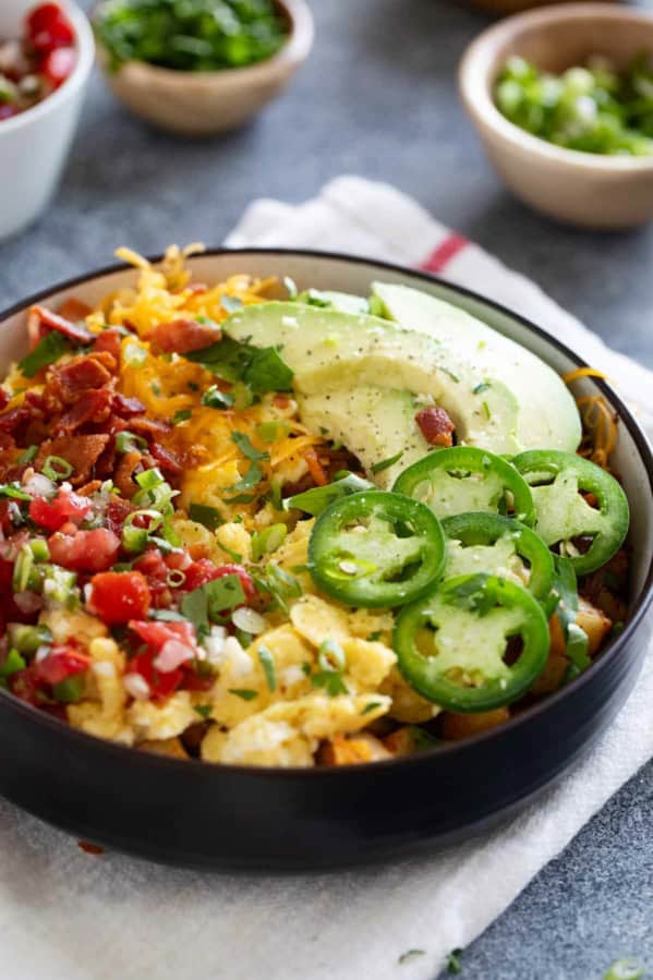 Loaded breakfast bowl, with roasted potatoes, scrambled eggs, bacon, and lots of toppings.