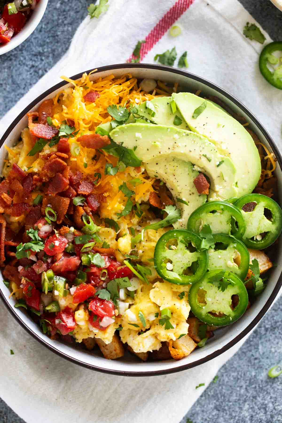 Breakfast bowl with potatoes, eggs, bacon, avocado, jalapeno, and more.